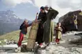 Szene des traditionellen Lebens im Gebirge: Frauen und Kinder in traditioneller Kleidung bei der Arbeit im Freien vor einem Bergpanorama.