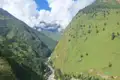 Panoramablick auf ein grünes Tal mit einem Fluss, umgeben von bewaldeten Bergen.
