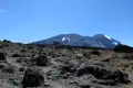Wanderer tragen Gepäck auf einem felsigen Pfad in Richtung des schneebedeckten Berggipfels.