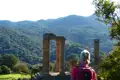 Besucher bewundert antike Säulen inmitten einer hügeligen Landschaft.