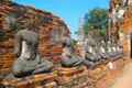 Verwitterte Buddha-Statuen vor einer Ziegelmauer in einer historischen Tempelanlage.