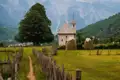 Eine kleine Kirche und Heuhaufen in einer Berglandschaft.