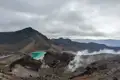 Türkisfarbener Kratersee und vulkanische Dämpfe in einer Berglandschaft.