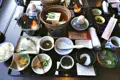 Traditionelles japanisches Frühstück mit verschiedenen Speisen wie Fisch, Tofu, Suppe, Reis und Beilagen.