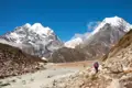 Wanderer auf einem Bergpfad neben einem Gletscherfluss, umgeben von schneebedeckten Gipfeln.