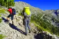Zwei Wanderer mit Trekkingausrüstung steigen einen Bergpfad hinauf.