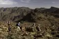 Wanderer mit Rucksäcken und Wanderstöcken in einer felsigen Berglandschaft.