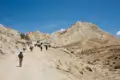 Wanderer und Packtiere auf einem Bergpfad in einer trockenen Landschaft.