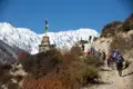 Wandergruppe auf einem Bergpfad im Himalaya mit Gebetsfahnen und schneebedeckten Bergen im Hintergrund.