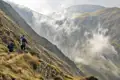 Zwei Wanderer mit Trekkingstöcken und Rucksäcken auf einem Bergpfad. Nebel steigt im Tal auf.