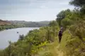 Wanderer auf einem Pfad entlang des Flusses. Ein Boot fährt im Hintergrund auf dem Wasser.