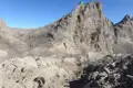 Wanderer auf einem felsigen Bergpfad, im Hintergrund ein imposanter Berggipfel.