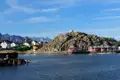Buntes Dorf an der Küste mit felsiger Insel und Bergen im Hintergrund.