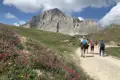 Wanderer mit Wanderstöcken auf einem Bergpfad. Im Hintergrund erhebt sich ein felsiger Gipfel.