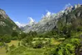 Panoramablick auf ein Gebirgstal mit üppiger Vegetation im Vordergrund und hohen, felsigen Gipfeln im Hintergrund.