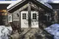 Eingangsbereich einer Holzhütte mit verschneitem Dach und Holzterrasse.