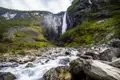 Spektakulärer Wasserfall, der über eine steile Felswand in einen schnell fließenden Fluss stürzt.