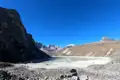 Panorama eines Bergsees im Himalaya mit Blick auf das felsige Ufer und die schneebedeckten Gipfel im Hintergrund.
