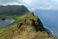 Spektakulärer Blick auf einen Kratersee, umgeben von grünen Feldern, der an einer steilen Klippe zum Meer hin abfällt.