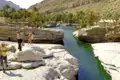 Reisende in einer Schlucht mit einem Flusslauf zwischen weißen Felsformationen und Palmen im Hintergrund.