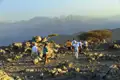 Wandergruppe auf einem felsigen Bergpfad mit Blick auf eine Bergkette und das Meer.