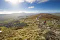 Wanderer auf einem Bergpfad mit Steinmauer und Talblick.