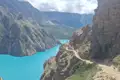Wanderer auf einem schmalen Pfad entlang eines türkisfarbenen Bergsees, umgeben von steilen Felswänden.