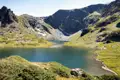 Bergsee mit umliegenden grünen Hängen und felsigen Gipfeln.