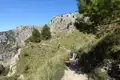 Wanderer auf einem Bergpfad mit felsigen Hängen im Hintergrund.