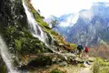 Wanderer auf einem Bergpfad neben einem Wasserfall in den Bergen.