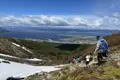 Wandergruppe auf einem Bergpfad mit Blick auf die Küste. Schnee liegt noch am Wegrand.