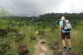 Wanderer auf einem Naturpfad, umgeben von Vegetation und mit Blick auf bewaldete Hügel.