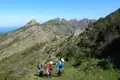 Drei Wanderer auf einem Bergpfad. Im Hintergrund sind felsige Gipfel und das Meer zu sehen.