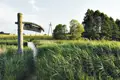 Hölzerner Wegweiser und Steg inmitten von hohem Gras.