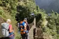 Zwei Wanderer mit Rucksäcken überqueren eine Hängebrücke im Gebirge.