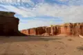 Rote Felsformationen und sandiger Boden unter einem bewölkten Himmel.