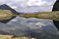 Idyllischer Bergsee mit Spiegelung der Wolken und einer Berghütte am Ufer.