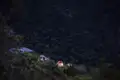 Beleuchtete Zelte am Rande eines dichten Waldes in der Abenddämmerung.