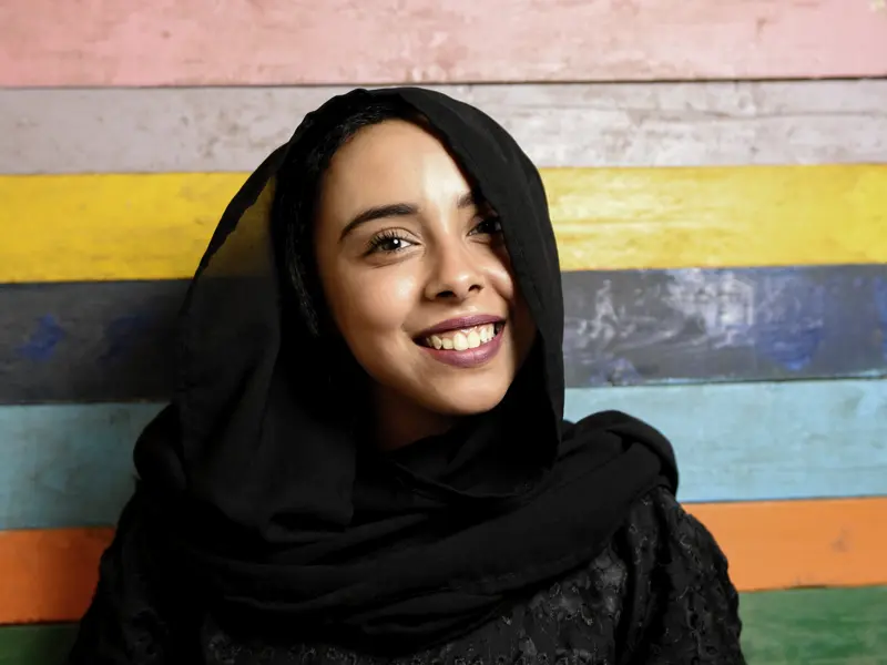 Junge Frau aus dem Oman mit schwarzem Kopftuch vor bunter Wand