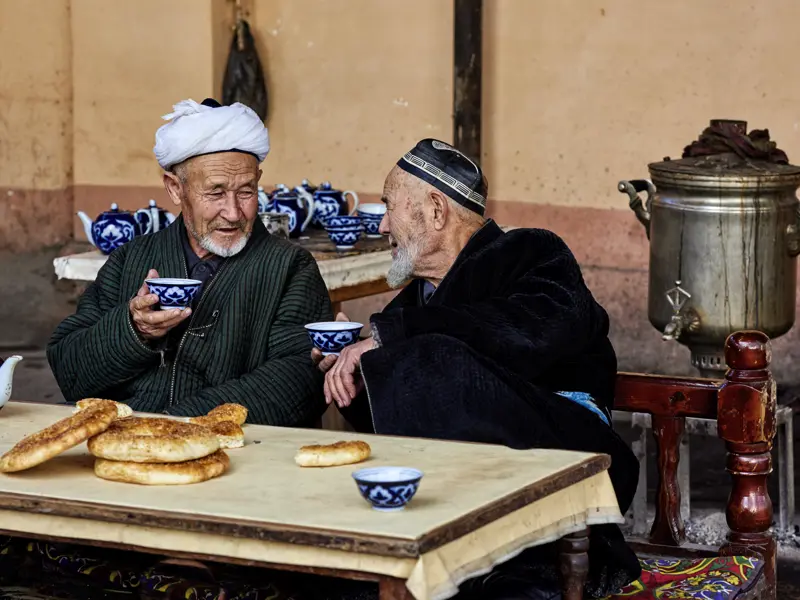 Auf unserer Studienreise Usbekistan - Höhepunkte sehen wir einheimische alte Männer, beim Teetrinken ins Gespräch vertieft. Die blauen Teeschälchen mit Baumwollmuster sind typisch für Usbekistan, die kreisrunden Fladenbrote ebenso.