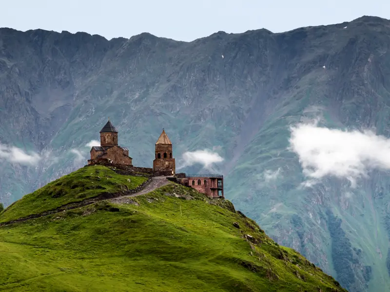 Vor den gewaltigen Bergflanken des Kaukasus erscheint uns auf unserer Rundreise durch Georgien die Gergeti-Dreifaltigkeitskirche winzig klein.