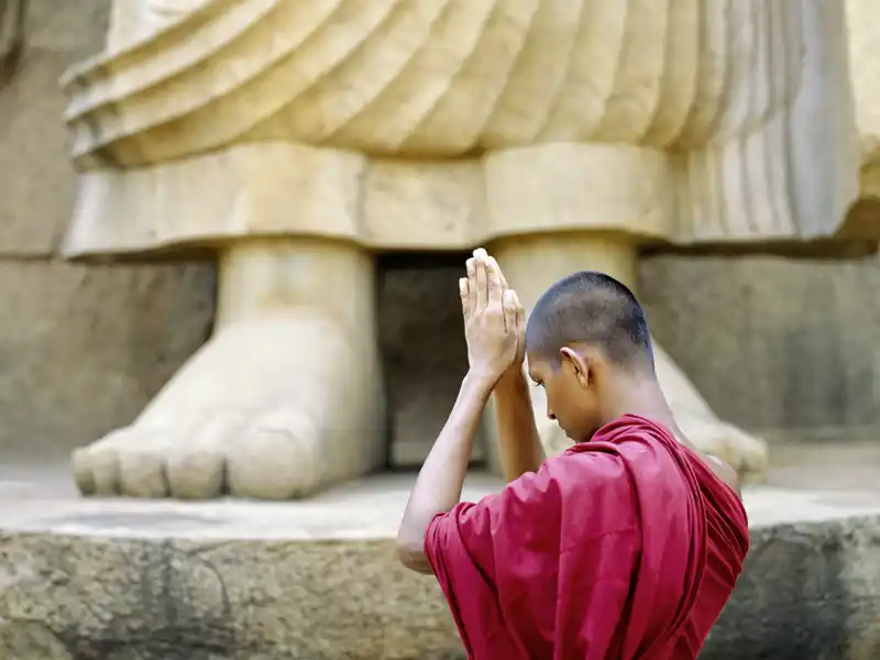 Auf unserer Reise nach Sri Lanka begegnen wir betenden Mönchen, die wie hier am Riesenbuddha von Aukana Buddhas sanfte Lehre praktizieren.