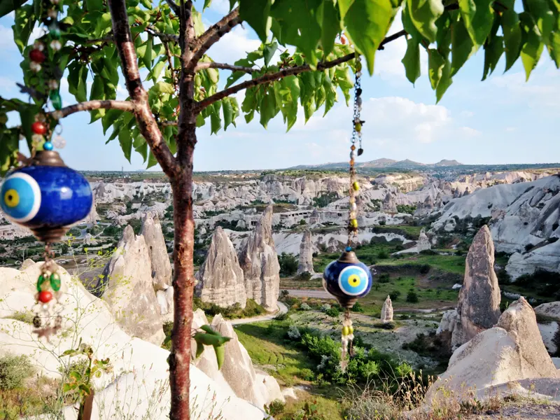 Magische Momente gibt es auf dieser achttägigen Kappadokien-Studienreise zuhauf. Hier der Blick auf die Feenkamine und die märchenhafte Welt im Nationalpark Göreme (UNESCO-Welterbe); im Vordergrund Glücksbringer, angelehnt an das Auge, das den bösen Blick abwehren soll.