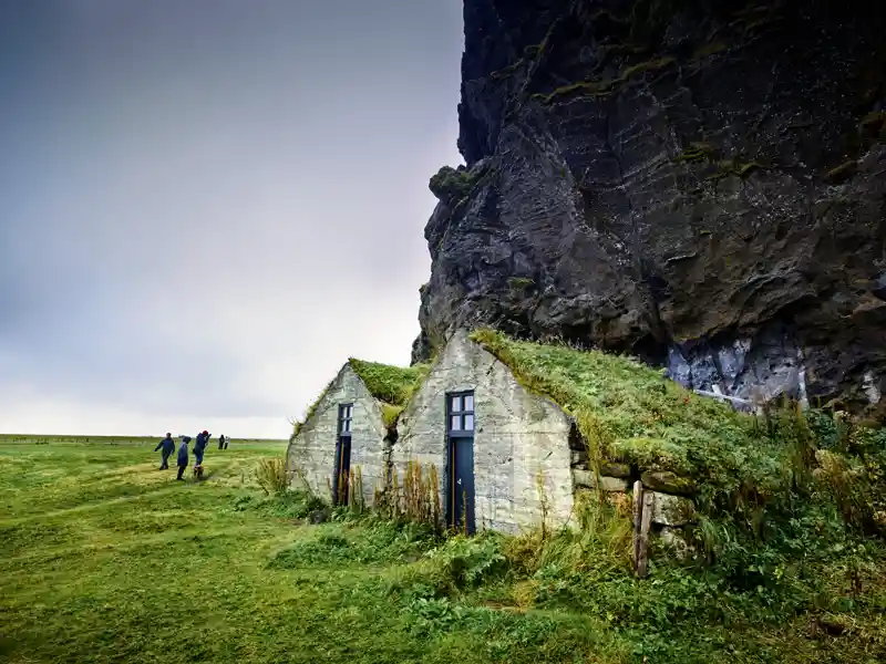 Auf unserer Studienreise durch Island bestaunen wir die in die Felswand gebauten Grassodenhäuser, die den Isländern über Jahrhunderte Schutz geboten haben.