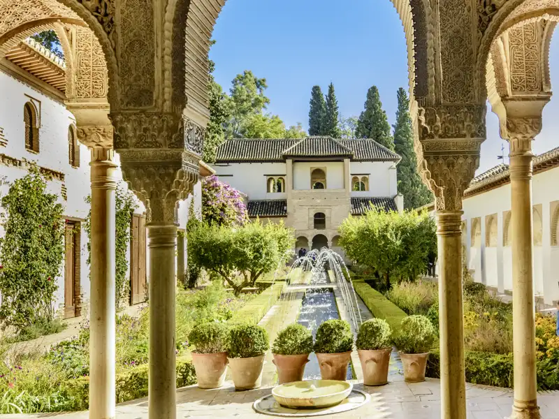 Die kunstvollen Bögen und Säulen der Alhambra rahmen den Blick auf den Garten und den Brunnen ein.
