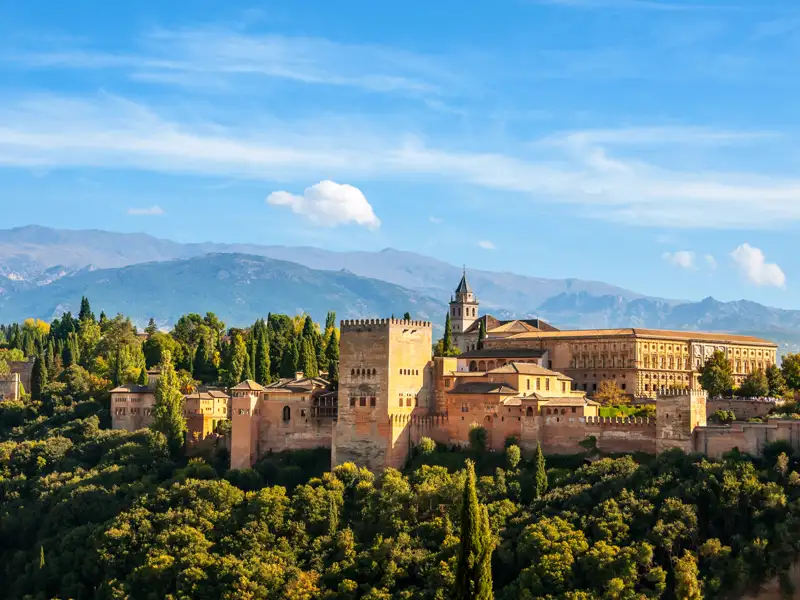 Auf unserer Reise bekommen wir einenPanoramablick auf die Alhambra mit ihren Türmen, Mauern und Gebäuden, eingebettet in die Landschaft der Sierra Nevada.