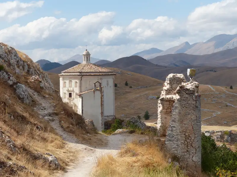 Historische Rundkirche und Burgruine inmitten einer bergigen Landschaft.