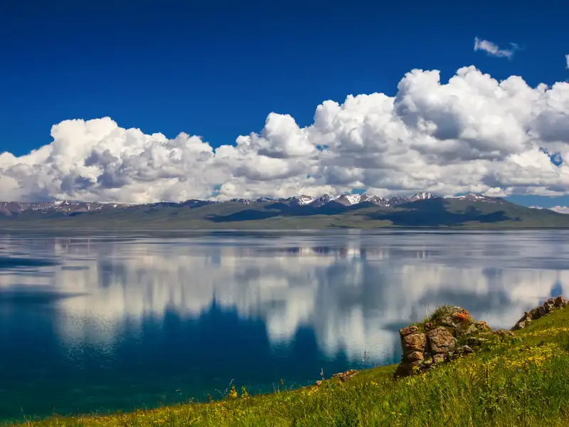 Ruhiger See mit Spiegelung der schneebedeckten Berge und Wolken.