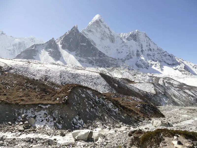 Schneebedeckte Bergkette mit einem Flussbett im Vordergrund, typisch für Hochgebirgsregionen.
