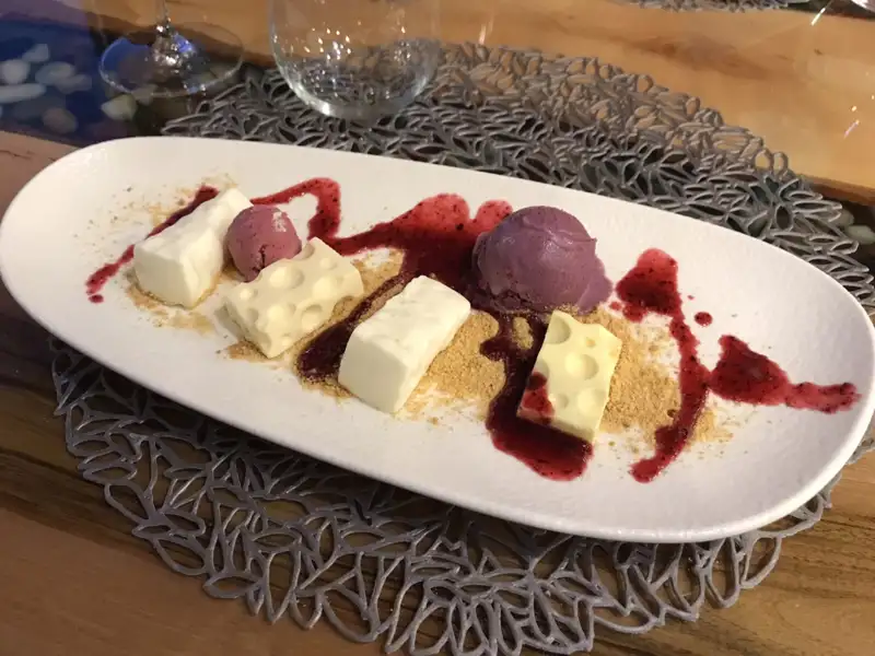 Käsekuchen-Dessert mit Sorbet und Beerensoße, serviert auf einem weißen Teller.